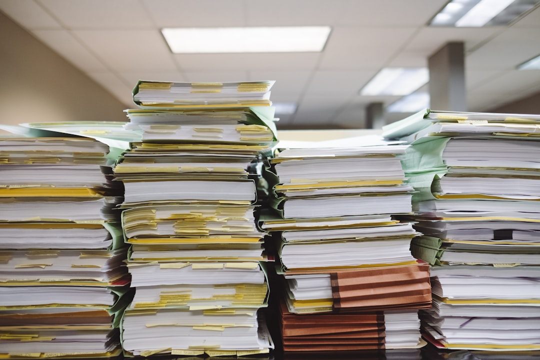Towering stacks of tabbed compliance files and folders in an office, representing the manual recertification paperwork burden in affordable housing