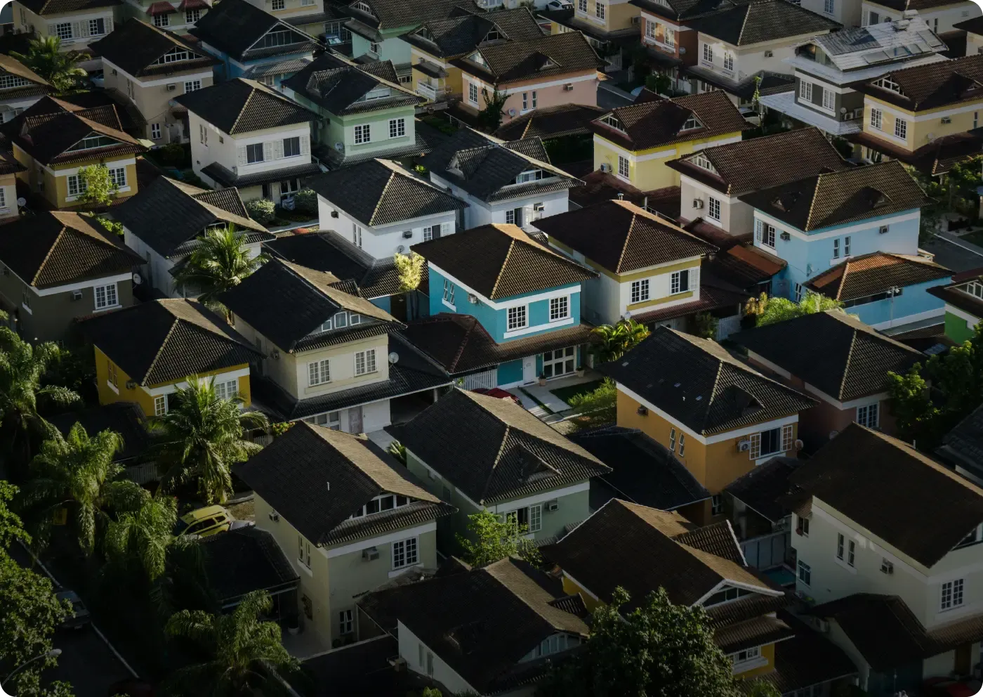 Aerial view of a residential neighborhood with closely spaced two-story houses featuring dark tiled roofs and various light-colored exteriors.