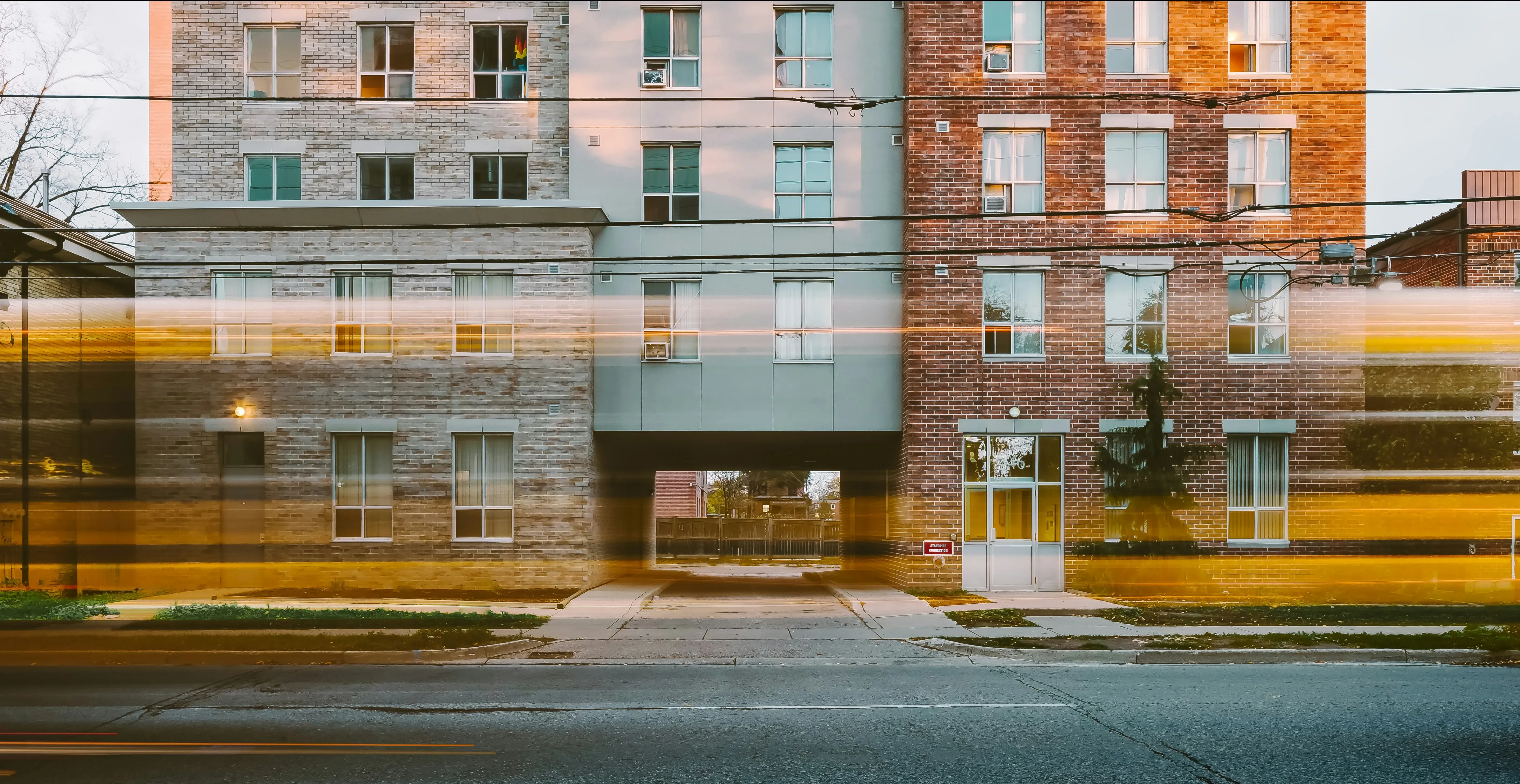 Long exposure of a street with light trails passing in front of a building with a passageway underneath.